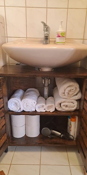 Badezimmer-Unterschrank mit Handtüchern, Toilettenpapier, Fön, Shampoo und Duschgel.